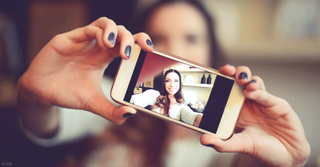 Woman taking a photo and debating if she's choosing plastic surgery for the right reasons