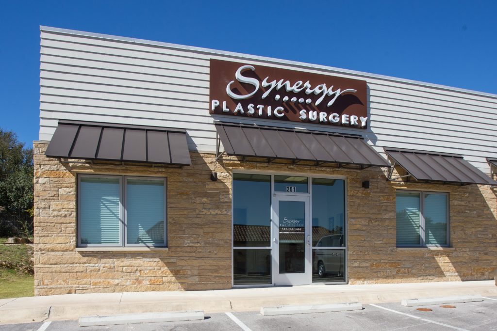 Entrance to Austin plastic surgery office  with large logo above a glass door surrounded by rock veneer walls