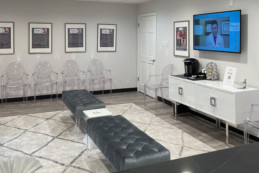 Waiting area of West Lake Hills office has black tufted benches with clear plastic chairs lining the walls and a flat-screen television.