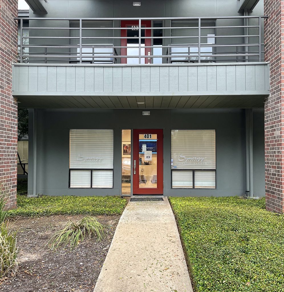 Front entrance to West Lake Hills plastic surgery office has a red door and grey walls with windows.