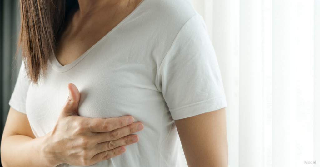 Woman wearing a white t-shirt feeling her breast with her right hand (model)