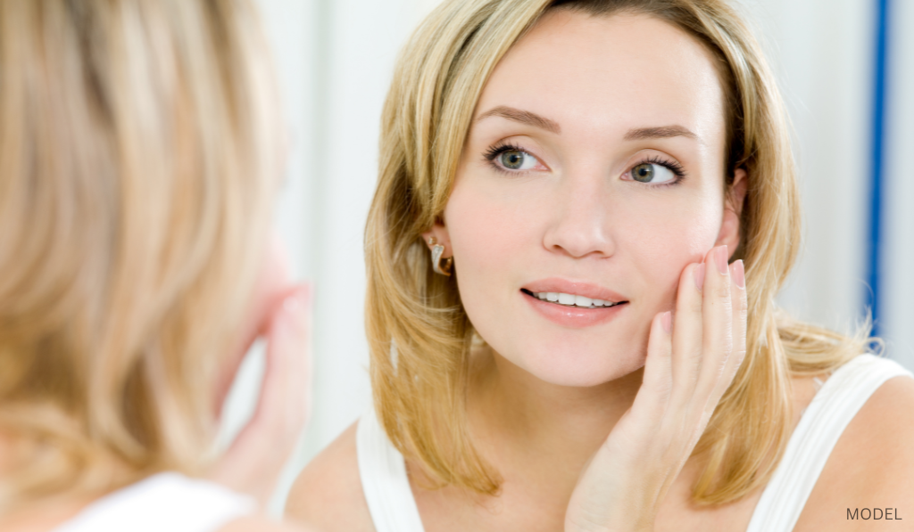 Woman looking at her reflection in the mirror and touching her face (model)