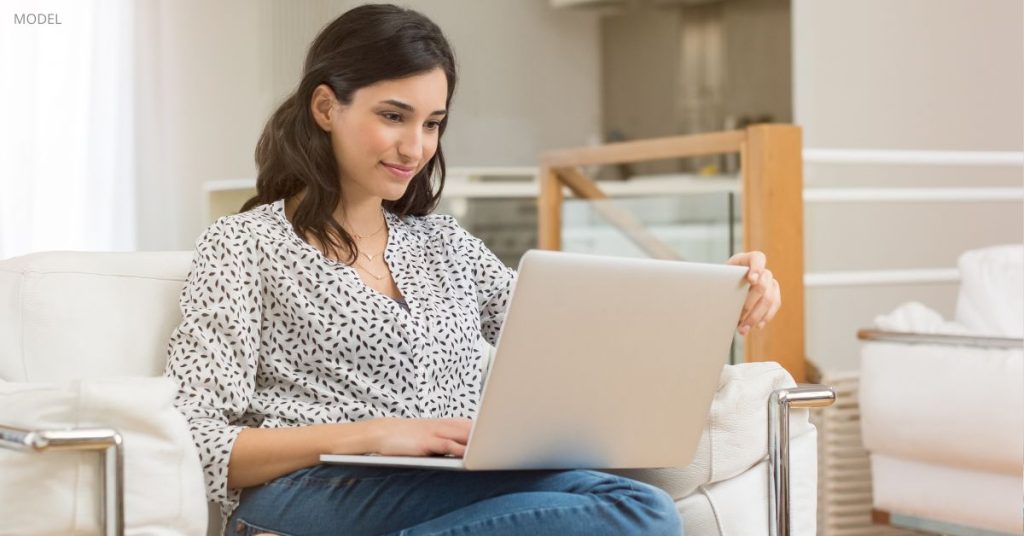Woman (model) sitting at home on laptop computer.