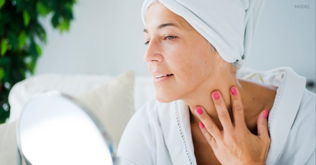 Woman with clear, youthful skin (model) looking in a stand mirror.