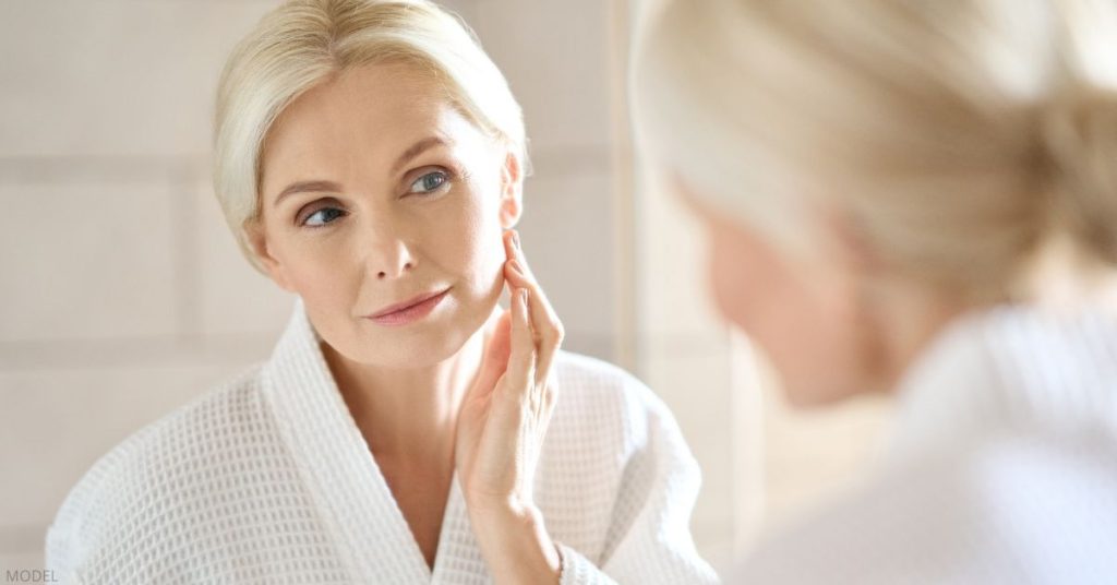 Woman looking in the mirror with hands on her face (MODEL)