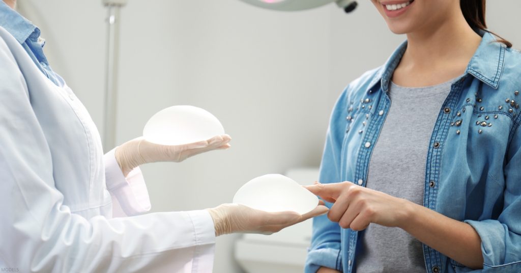 A doctor holds two breast implants while discussing options with a female patient (models).