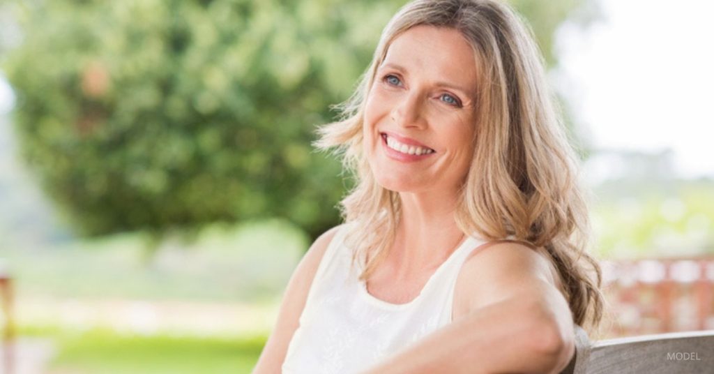 Woman (model) with a well-defined chin and neck shape sitting outside in a park.