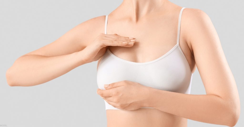 A woman wearing a white bra gently touches her chest (model)
